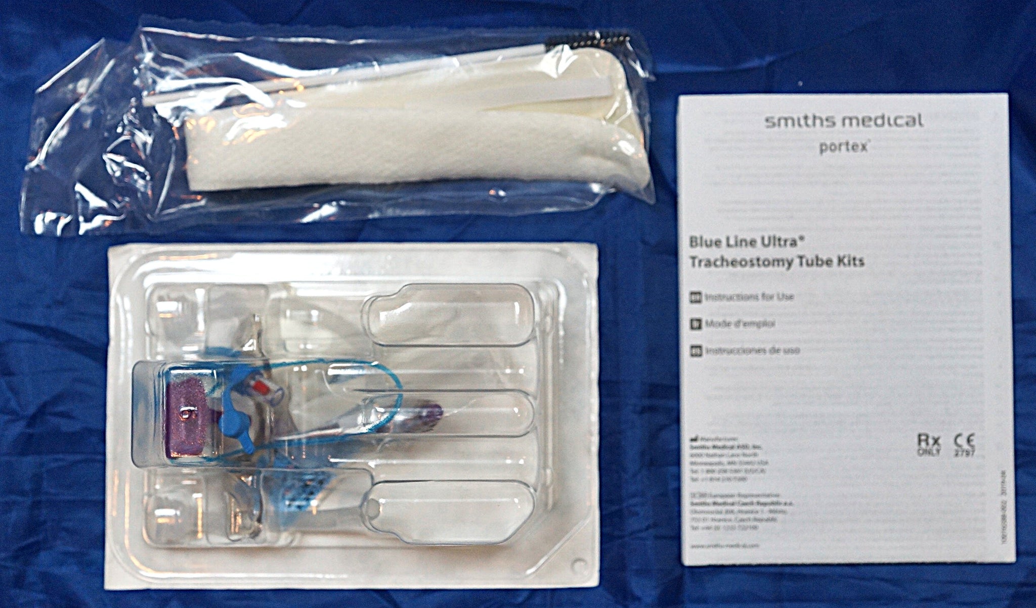 Smiths Medical Portex Blue Line Ultra Tracheostomy Tube Kits shown with its contents on a blue background, including a plastic-wrapped white tube, a clear plastic tray with tubes and accessories, and an instruction booklet.